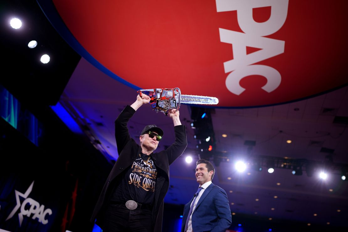 Elon Musk wields a chainsaw as he leaves the stage alongside Newsmax anchor Rob Schmitt at the Conservative Political Action Conference (CPAC) at the Gaylord National Resort Hotel and Convention Center on February 20, 2025, in Oxon Hill, Maryland.