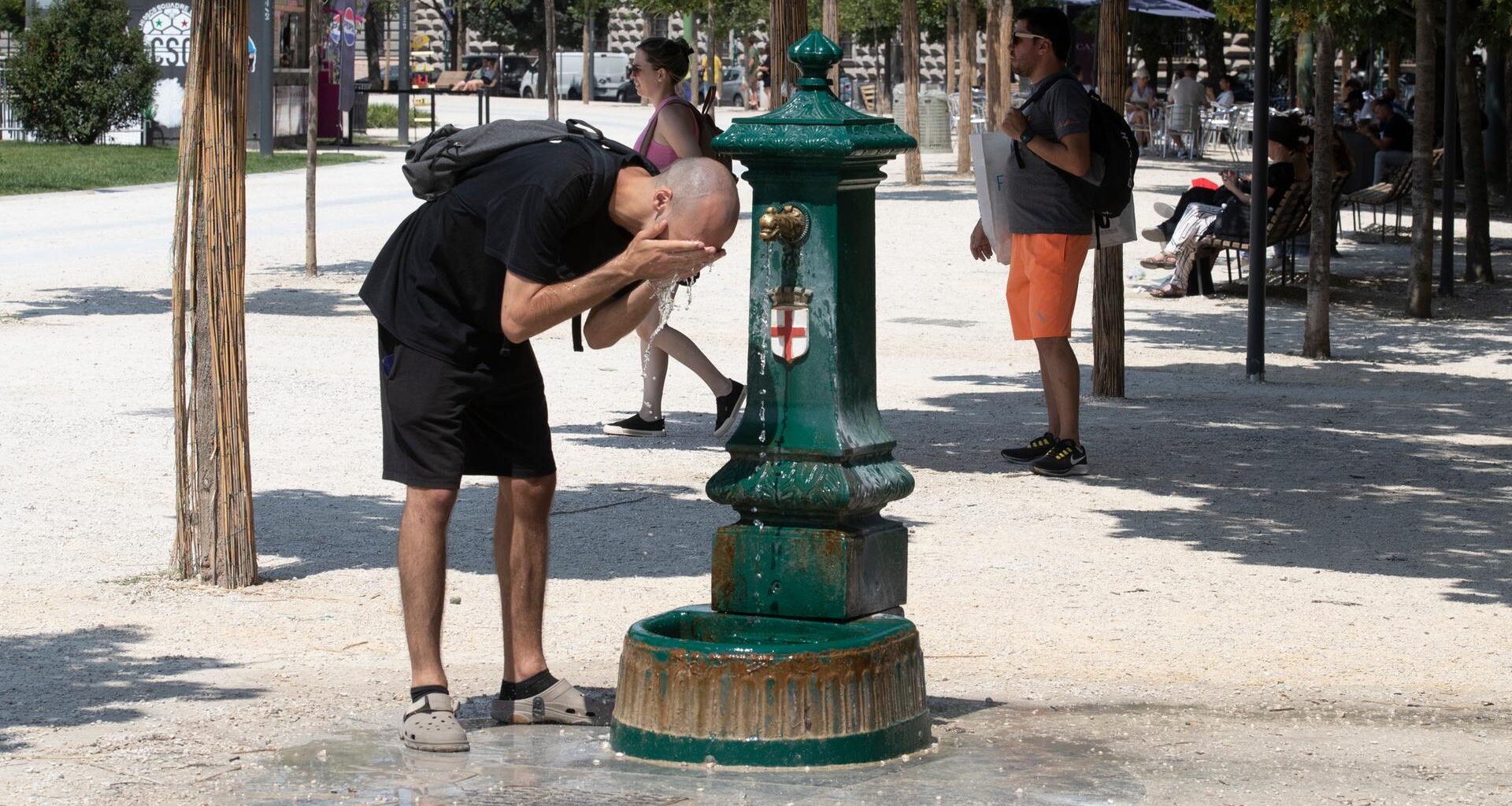 Ein Mann steht gebückt vor einem Trinkbrunnen und erfrischt sich mit dem kalten Wasser.