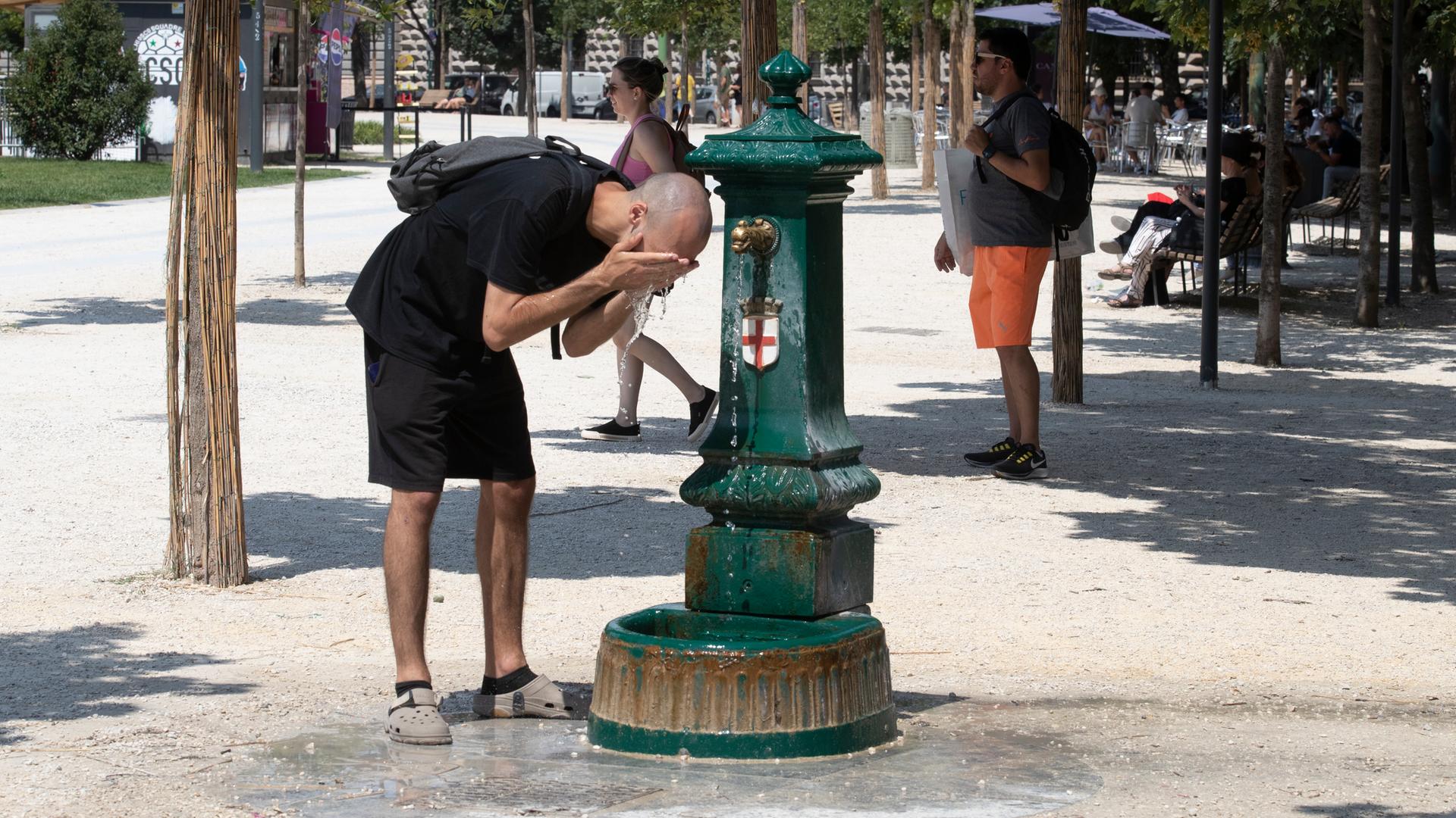 Ein Mann steht gebückt vor einem Trinkbrunnen und erfrischt sich mit dem kalten Wasser. Ein Mann steht gebückt vor einem Trinkbrunnen und erfrischt sich mit dem kalten Wasser.