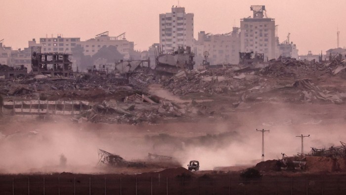 The small vehicle is surrounded by dust and the wreckage from bombed buildings