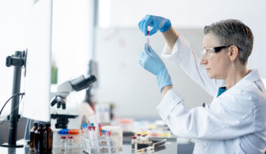 A female medical laboratory technician works independently as she analyzes plasma samples. She is wearing a lab coat as well as protective eyewear and gloves as she focuses on her task.