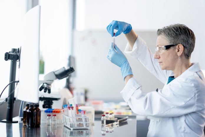 A female medical laboratory technician works independently as she analyzes plasma samples. She is wearing a lab coat as well as protective eyewear and gloves as she focuses on her task.