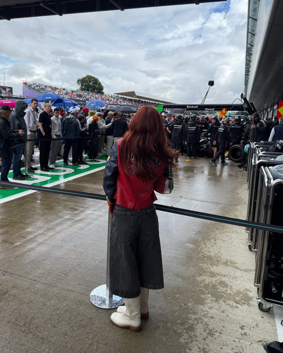a woman stands in front of an f1 race.