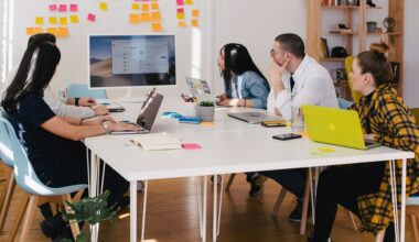 Five people at table watching screen of white computer monitor
