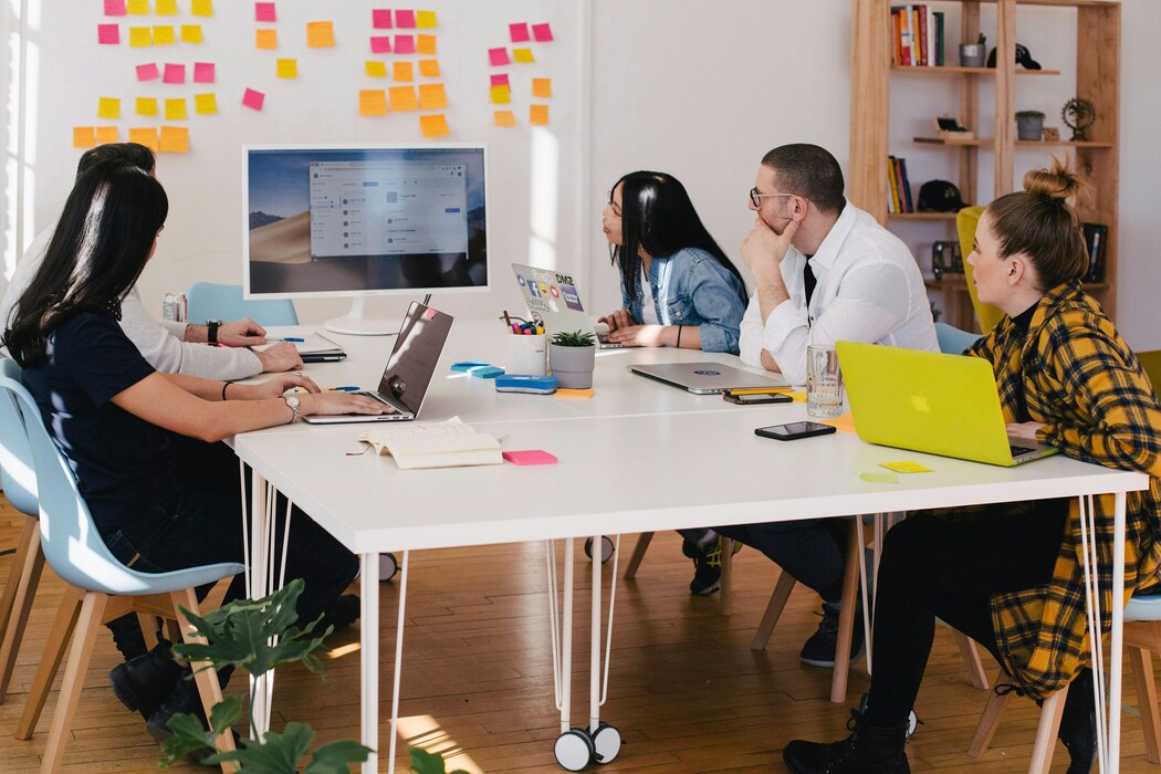 Five people at table watching screen of white computer monitor