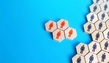 Four wooden blocks with red person icons on them separated from a larger group of wooden blocks with black person icons against a solid light blue background