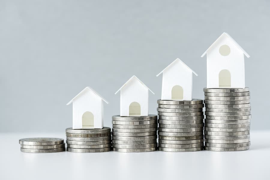 Small white wooden houses on top of increasingly large piles of silver coins