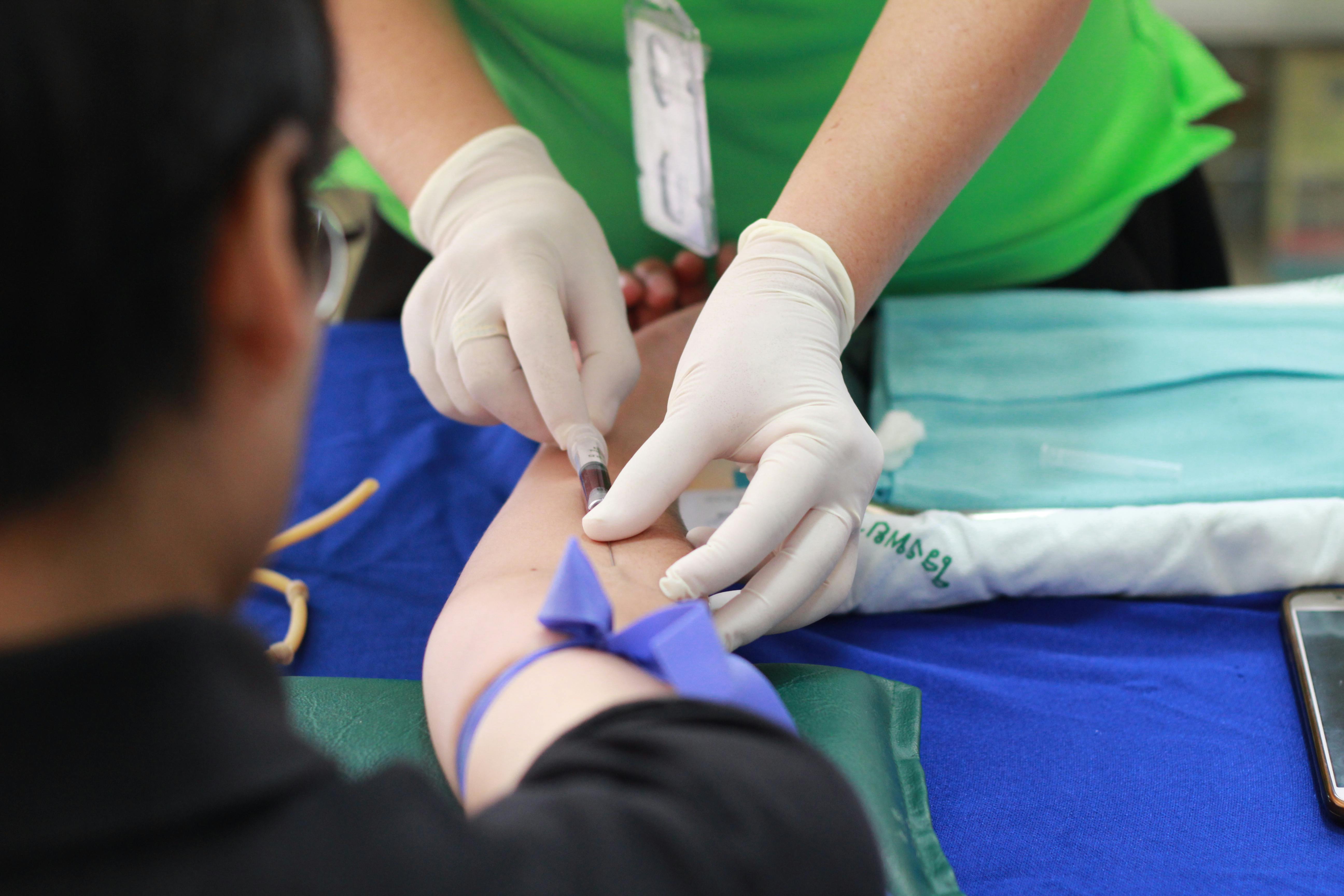 Healthcare worker drawing blood from a patient’s arm using a syringe while wearing gloves.