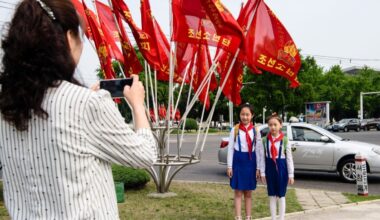 Pioneers in Pyongyang pose in front of North Korean flags