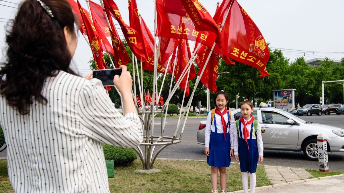 Pioneers in Pyongyang pose in front of North Korean flags