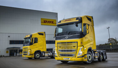 Two DHL eCommerce trucks sit parked outside a warehouse underneath a grey cloudy sky
