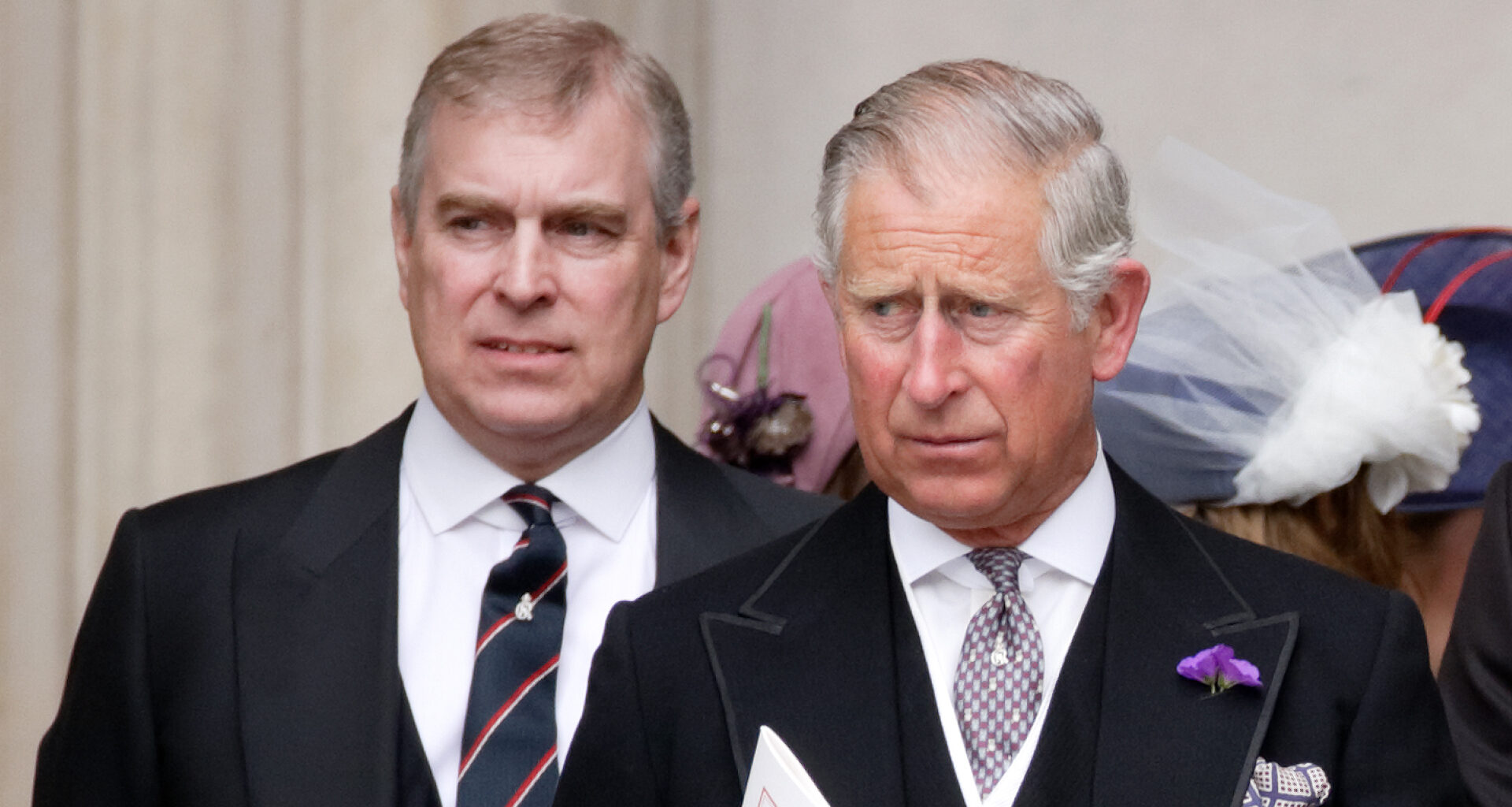 Prince Andrew wears a suit and stands behind King Charles
