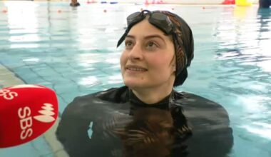 A swimming student at the edge of the pool speaks into a microphone.