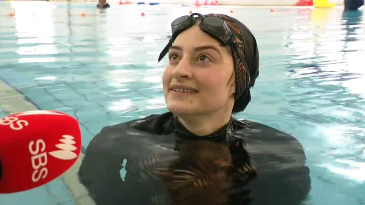 A swimming student at the edge of the pool speaks into a microphone.