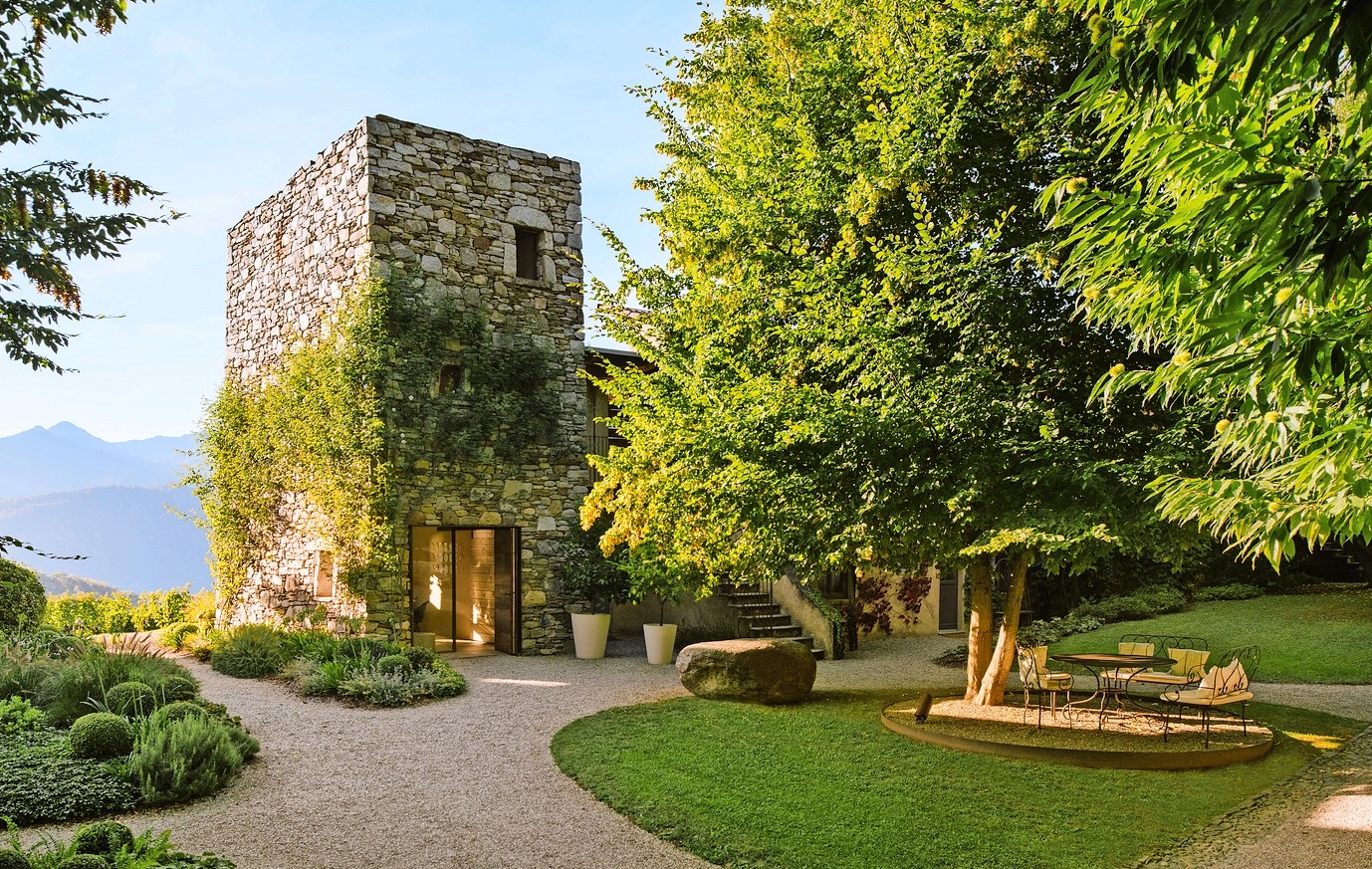 Stone building in a garden with mountains in the background.