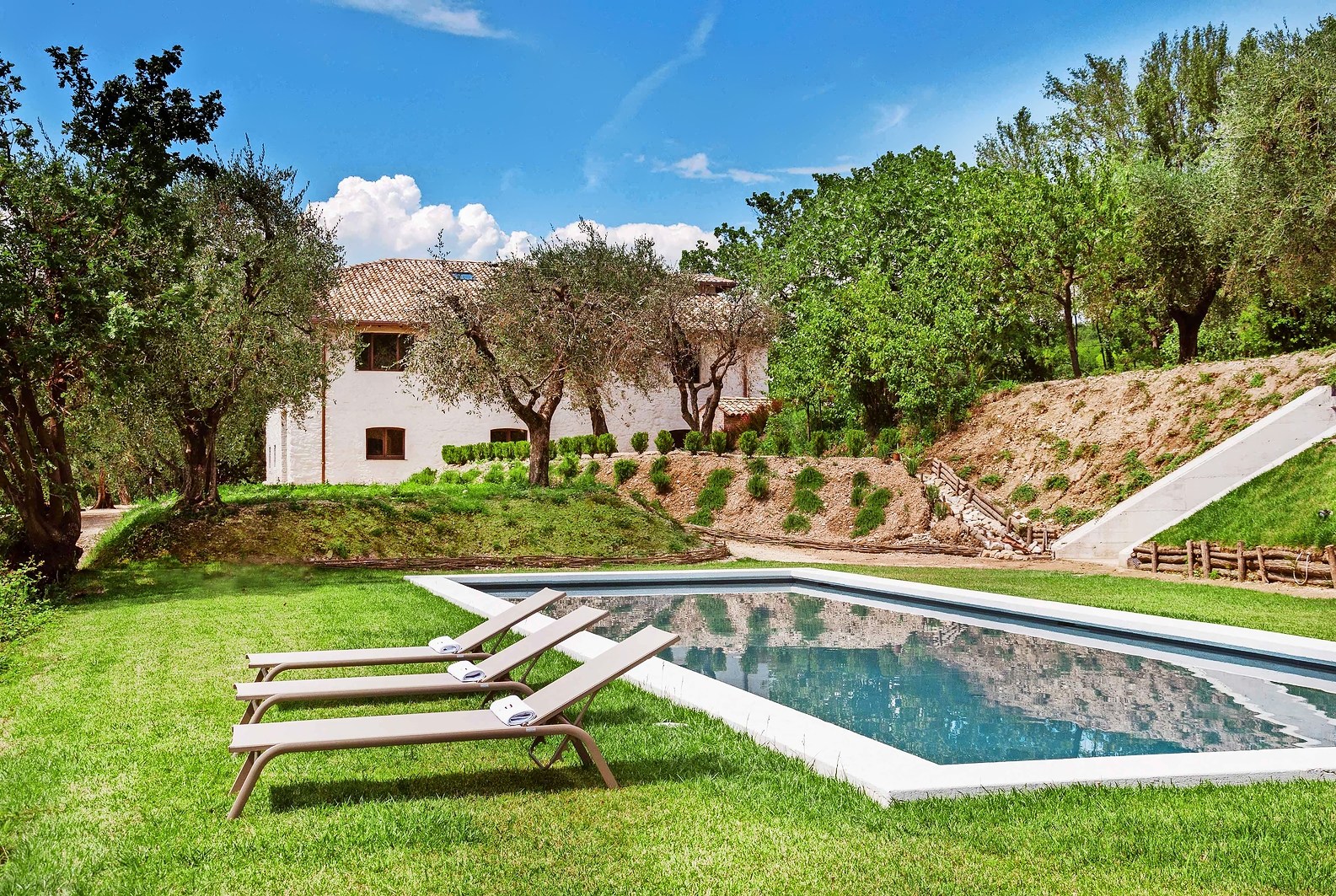 Rectangular pool with three lounge chairs and a white building in the background.