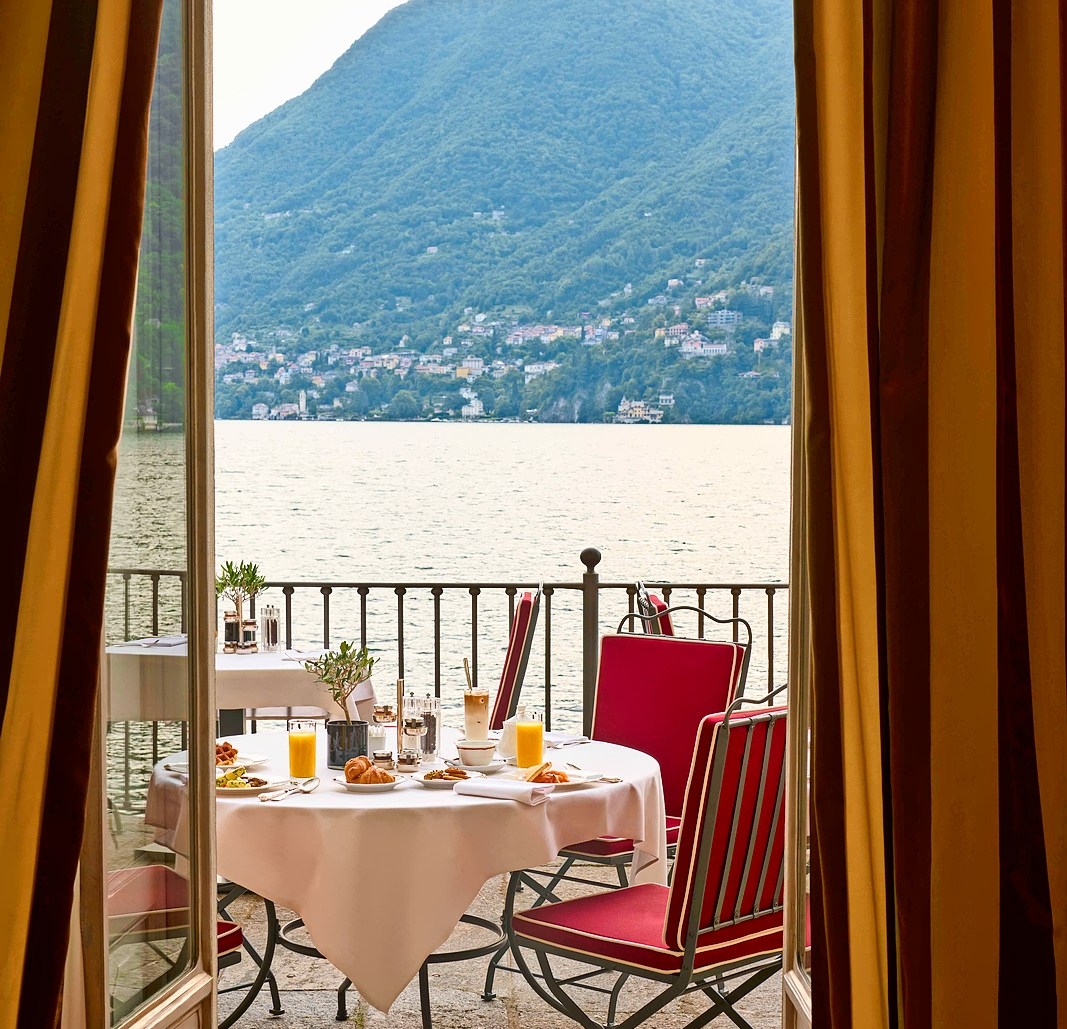 Breakfast table on a hotel balcony overlooking a lake and mountains.