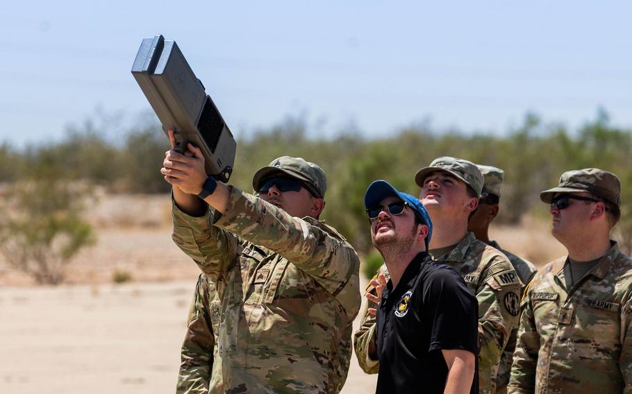 One soldier aims a large device at the sky with both hands as others look on.