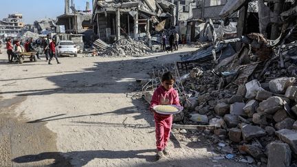 Une fillette palestinienne ramène de la nourriture distribuée par l'ONG World Central Kitchen à Khan Younès, dans la bande de Gaza, le 16 mars 2025. (ABED RAHIM KHATIB / ANADOLU / AFP)