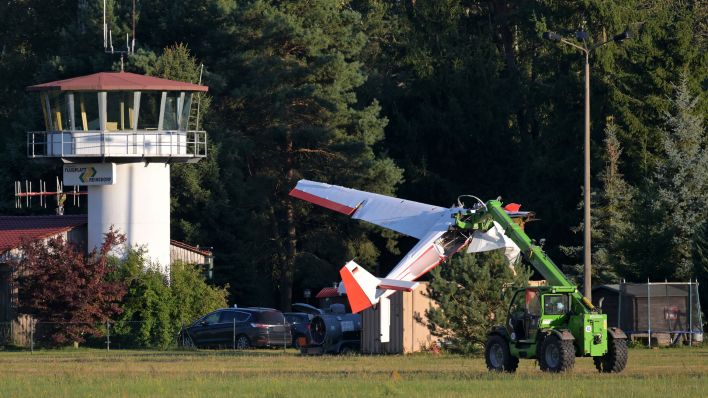 Das abgestürzte Flugzeug wird von einem Kran abtransportiert, im Hintergrund ist der Tower des Flugplatzes zu sehen. Bild: Michael Bahlo/dpa