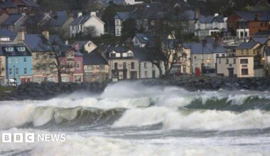 In the foreground, large waves. In the background, a row of houses.