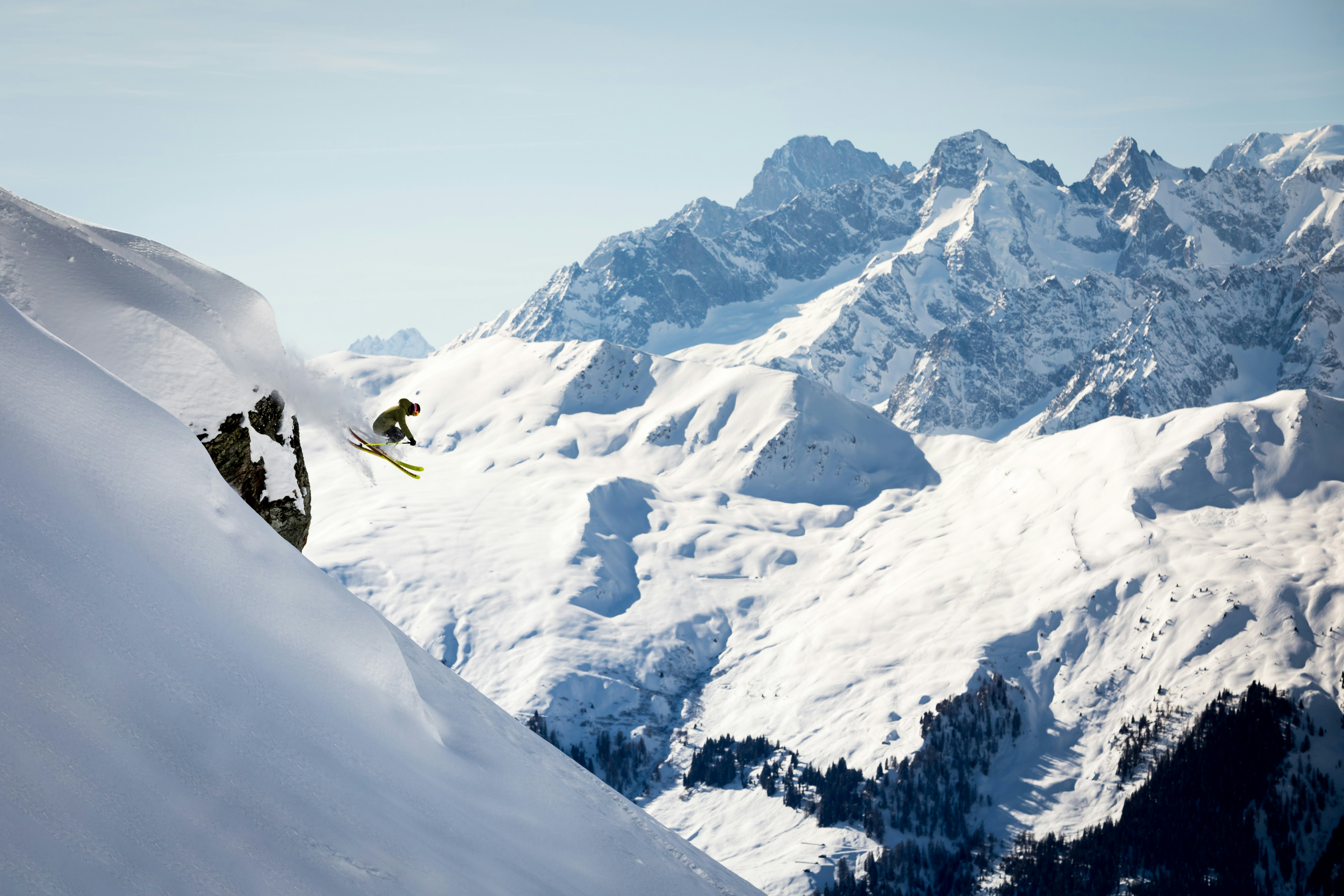 A skiier is airborne on a slope with snowy mountains in the background