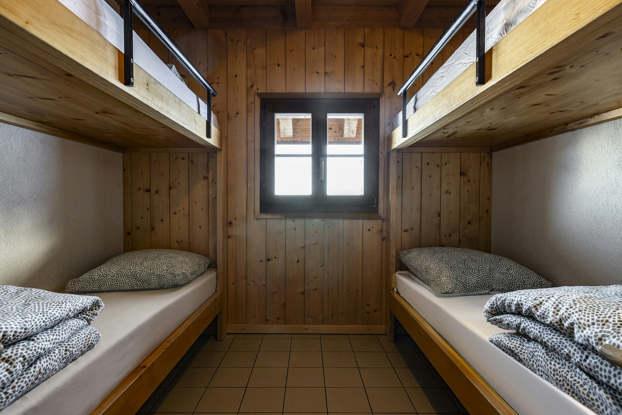 Two sets of bunk beds flush against the walls on opposite sides of a room with a wood-paneled wall that has a window