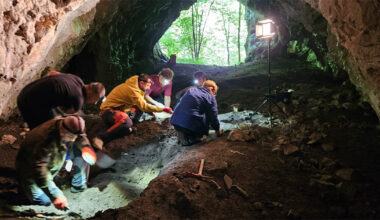seis pessoas agachadas trabalhando com ferramentas na escavação do solo no interior de uma caverna