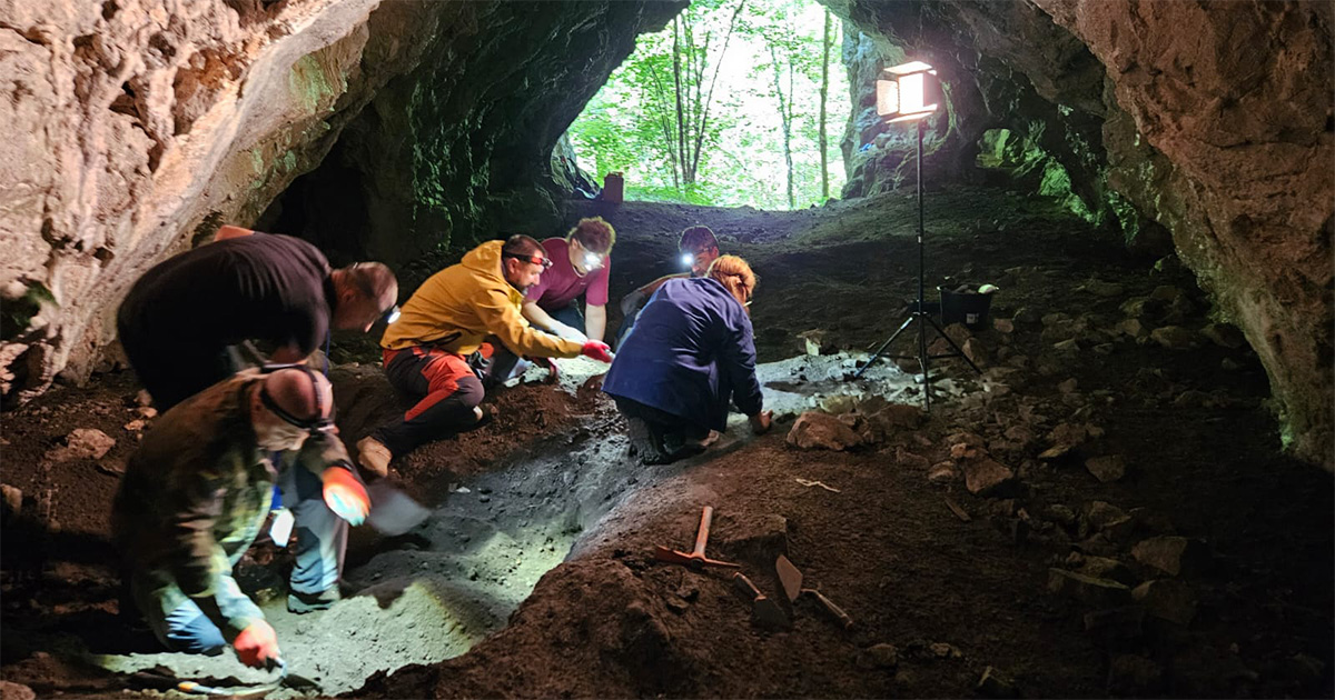 seis pessoas agachadas trabalhando com ferramentas na escavação do solo no interior de uma caverna