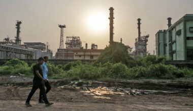 Pedestrains walk past an oil refinery in Mumbai, India.