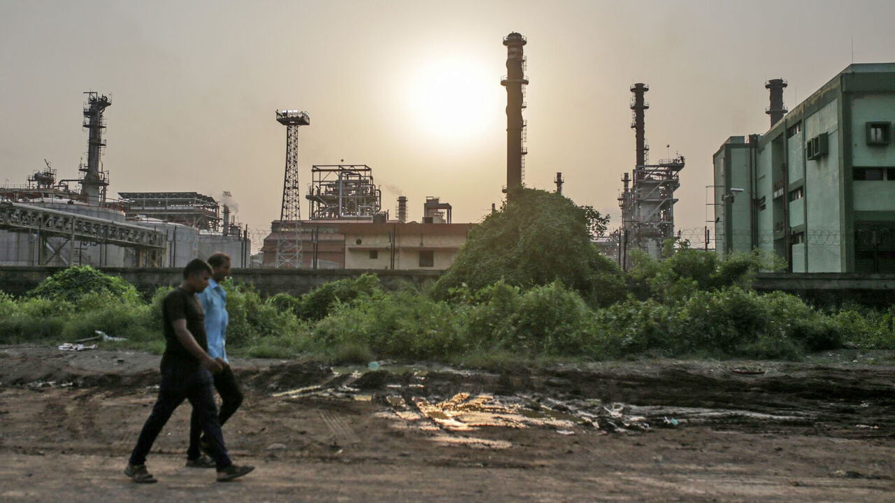 Pedestrains walk past an oil refinery in Mumbai, India.