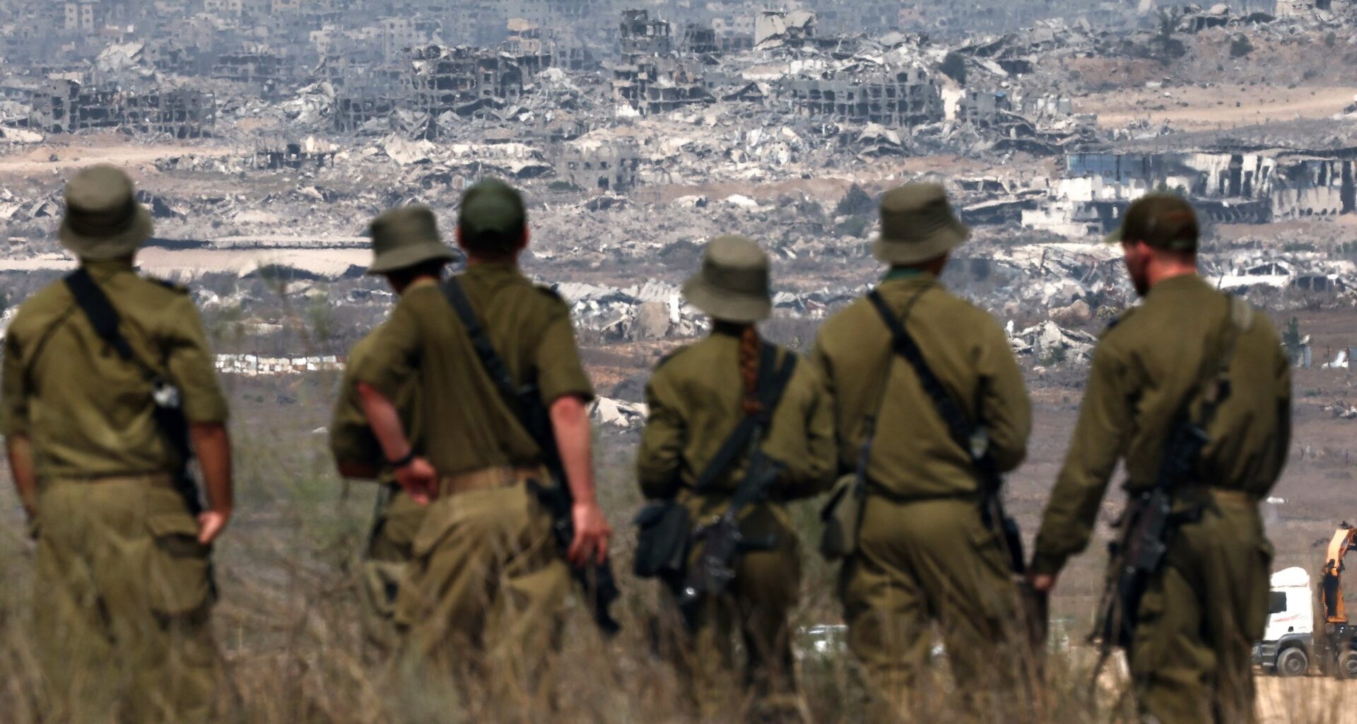 Israeli soldiers look at destroyed buildings in the Gaza Strip as they stand on the border with the Palestinian territory, on August 13, 2025.