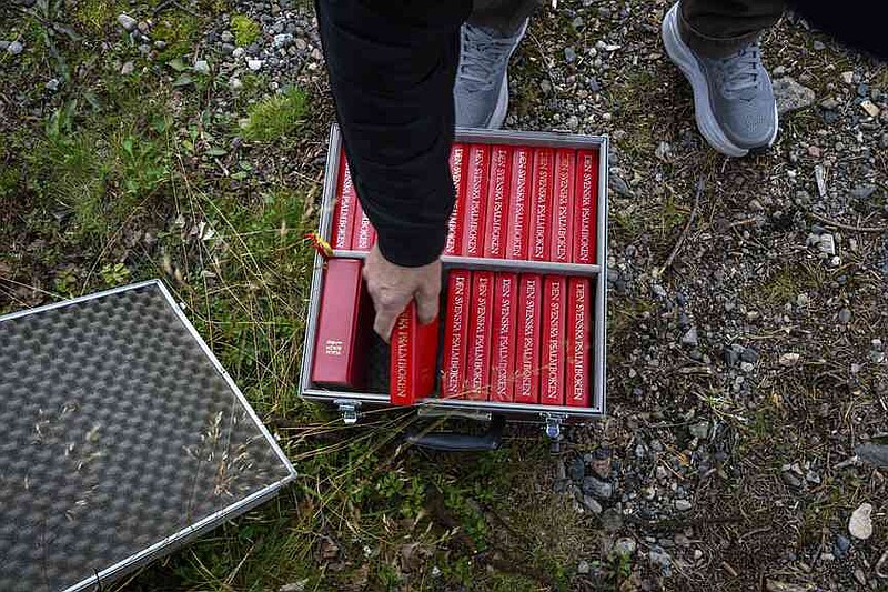 A person handles a hymnal during an outdoor prayer for the move of the Kiruna Church, a Sami style wooden Swedish Lutheran church, called Kiruna Kyrka in Swedish, in Kiruna, Sweden, Sunday, Aug. 17, 2025, two days before its move along a 5-kilometer (3-mile) route east to a new city center as part of the town's relocation. (AP Photo/Malin Haarala)