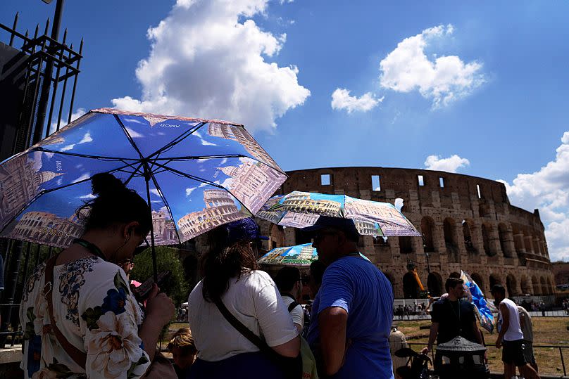 Tourists use umbrellas to shelter from the heat as they line up for a tour of the Forum in Rome, on Tuesday, July 22, 2025.