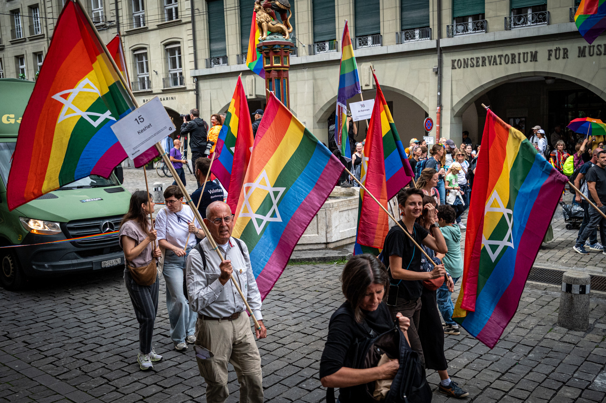 Menschen bei einer Parade in Bern mit Regenbogenflaggen, die den Davidstern zeigen, im Hintergrund ein historisches Gebäude. Menschen bei einer Parade in Bern mit Regenbogenflaggen, die den Davidstern zeigen, im Hintergrund ein historisches Gebäude.