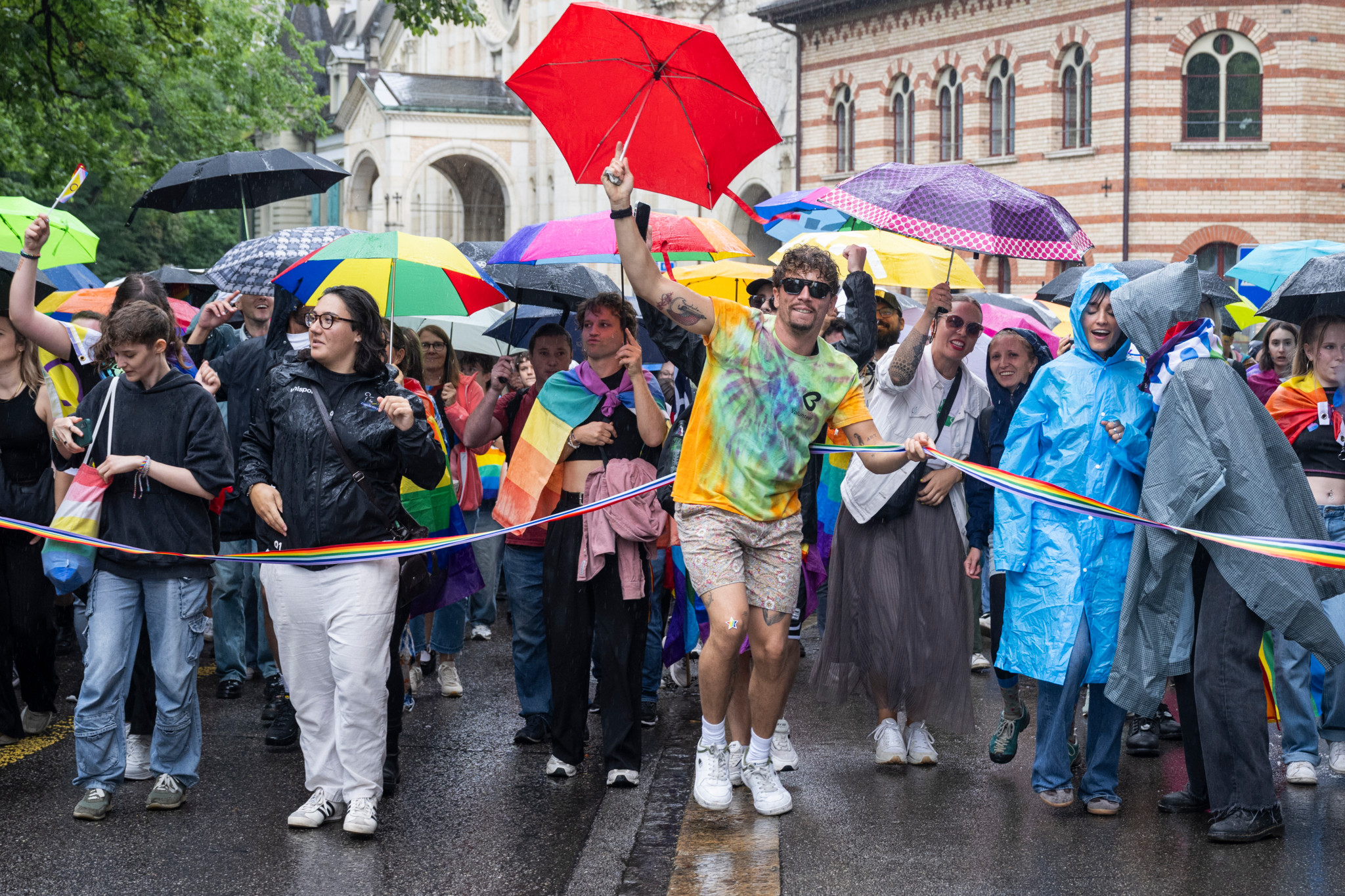Teilnehmer der BernPride 2025 in Bern mit bunten Regenschirmen und Regenjacken, trotz Regen fröhlich feiernd. Teilnehmer der BernPride 2025 in Bern mit bunten Regenschirmen und Regenjacken, trotz Regen fröhlich feiernd.
