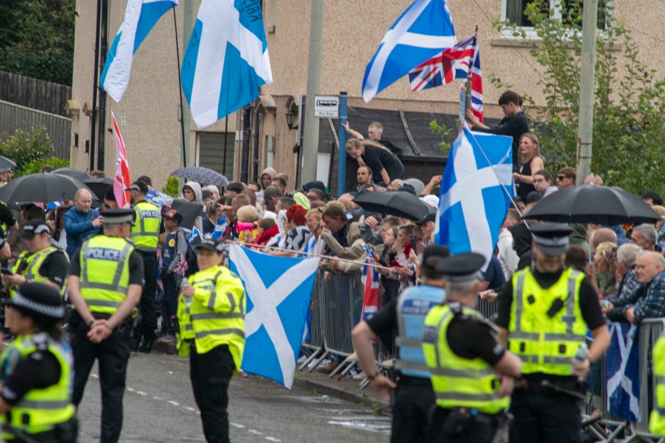 Protest in Falkirk with police and Scottish flags.