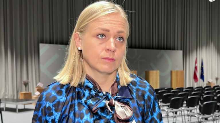 Elina Valtonen is interviewed by Yle. In the background is a conference hall with a speaker's podium and many empty chairs.