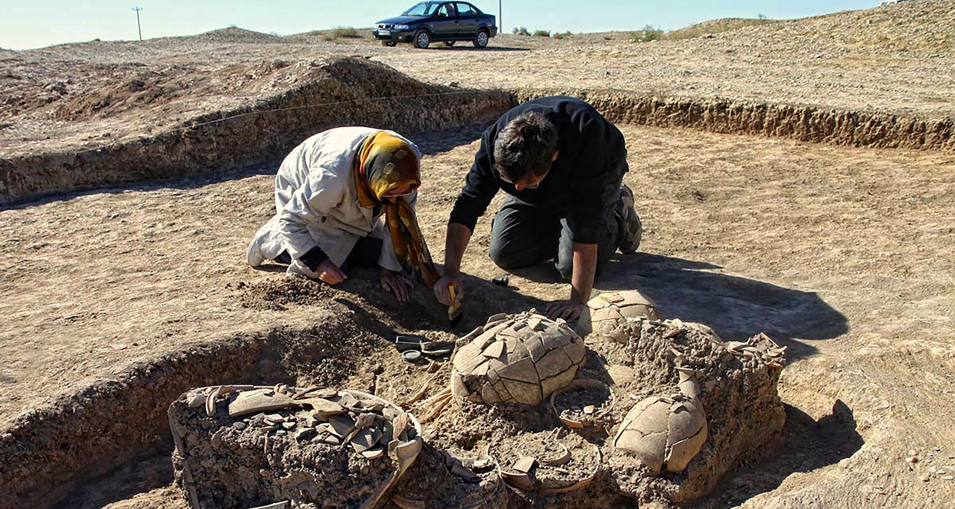 two archaeologists remove goods from an excavated grave in the desert