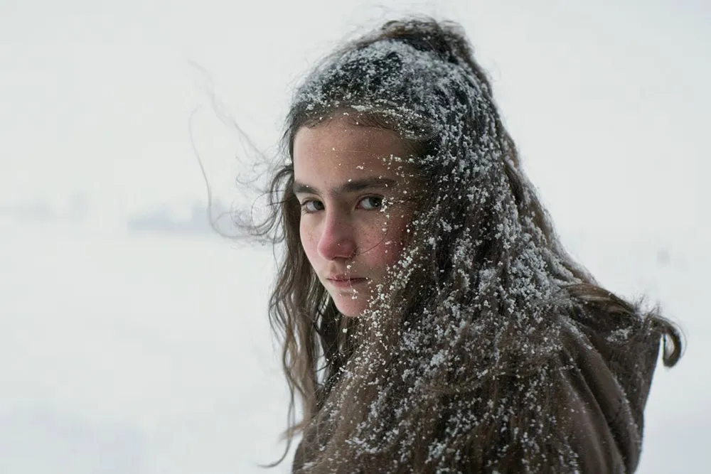 A girl with snow in her hair looks a the camera.