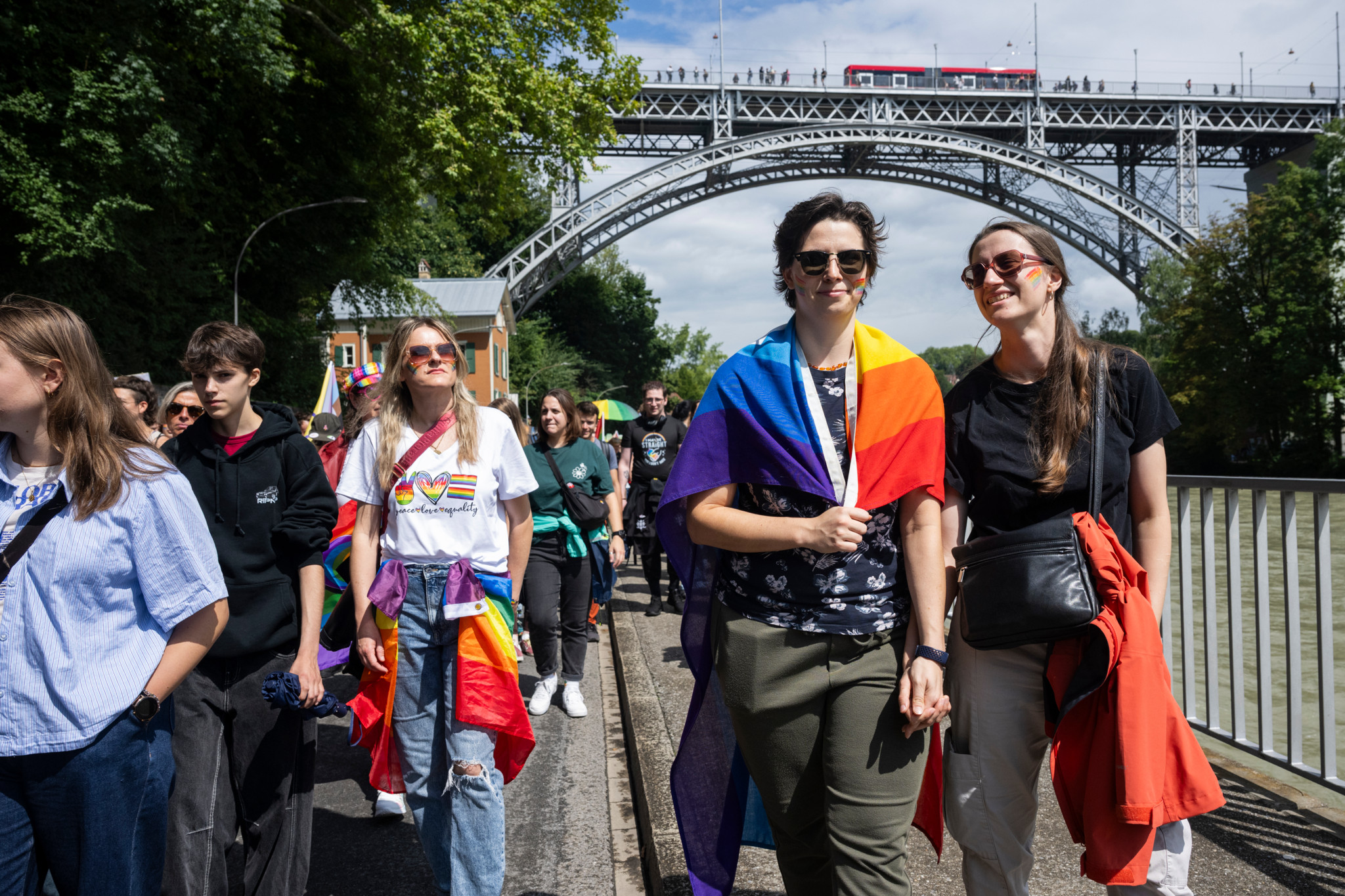 Teilnehmer der BernPride 2025 spazieren fröhlich unter einer Brücke in Bern, einige mit Regenbogenfahnen bekleidet. Teilnehmer der BernPride 2025 spazieren fröhlich unter einer Brücke in Bern, einige mit Regenbogenfahnen bekleidet.
