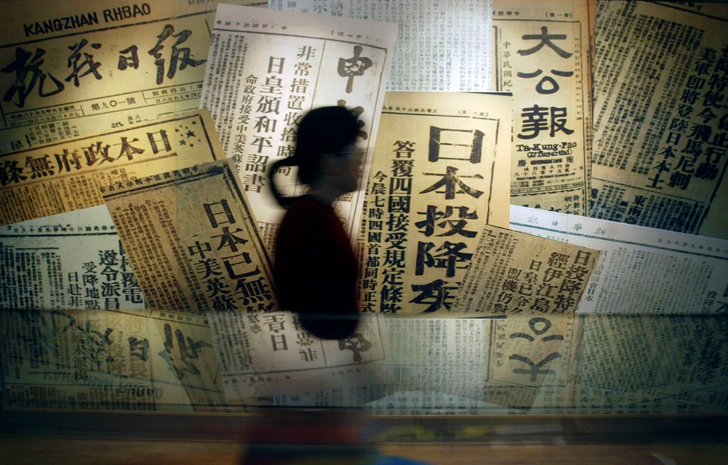A person with a ponytail is silhouetted against a museum exhibit showing newspapers with text in Chinese.