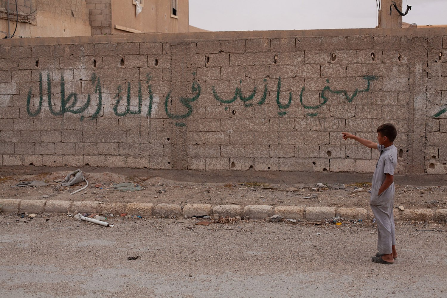 A boy points toward a wall with green text graffiti.