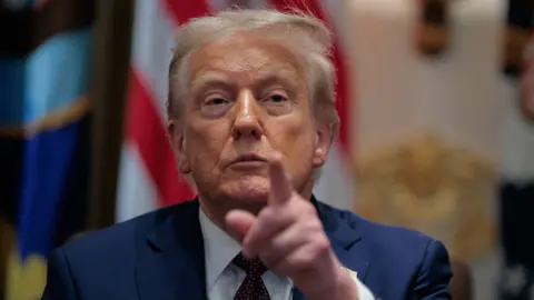 Getty Images Donald Trump points in the direction of the camera and wears a blue suit and tie. 