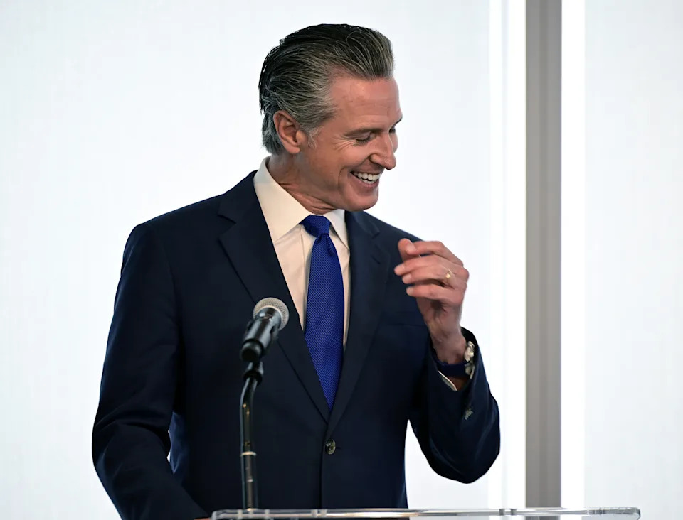 Man in a suit at a podium, smiling. Appears to be addressing an audience or preparing to speak