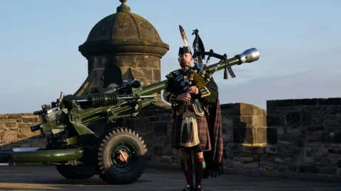 PA A bagpiper dressed in military uniform, including a kilt, playing at Edinburgh Castle as the sunrises