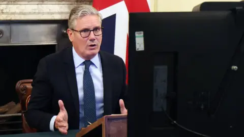 EPA Keir Starmer sitting at a desk in front of a fireplace and a union flag. In the foreground is the back of a computer.