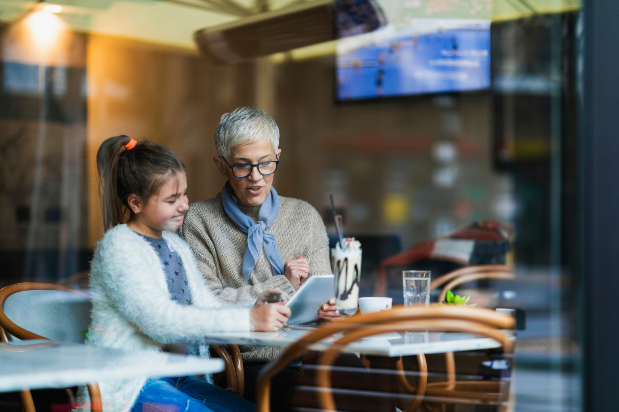Une petite fille et sa grand-mère utilisant une tablette dans un café, avec une boisson frappée sur la table. Une petite fille et sa grand-mère utilisant une tablette dans un café, avec une boisson frappée sur la table.