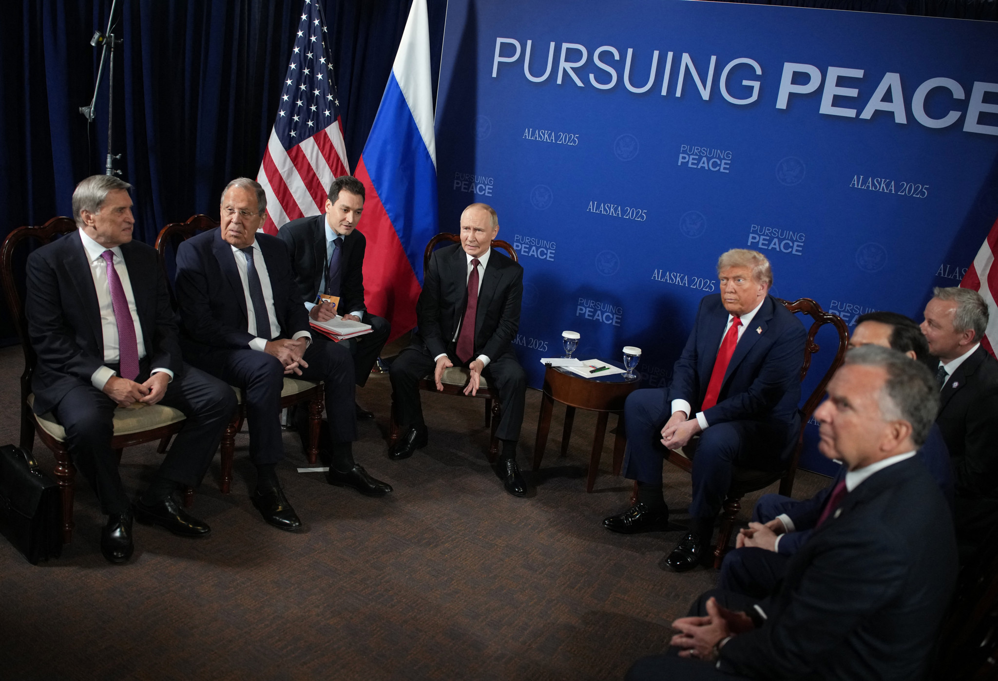 Rencontre entre Donald Trump, Vladimir Poutine, Sergey Lavrov et Marco Rubio à Anchorage en 2025 pour des pourparlers de paix sur l’Ukraine, avec drapeaux américain et russe en arrière-plan.
