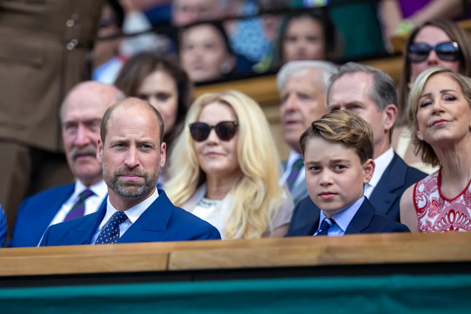 Prince George and Prince William sitting next to each other in blue suits at Wimbledon